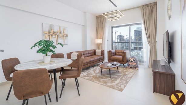 A modern living room with a round dining table, brown leather sofas, a coffee table, and a large window with a view of the city. - Jeewar Brand New Relaxing Pool Kids Area (Dubai)