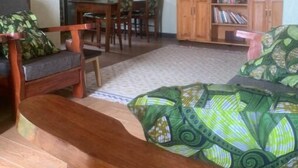 Ein Zimmer mit Holzboden, einem Esstisch mit Stühlen, einer Couch, einem Bücherregal und einer hängenden Pflanze.