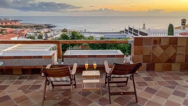 A terrace with a view of the sea, featuring a table with two chairs and two glasses of orange juice. - Surf-Check House - 3 min walk to the Beach (Playa del Hombre)
