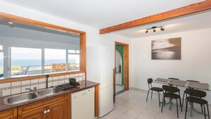 A modern kitchen with a large window, wooden cabinets, a dishwasher, and a dining area with chairs. - Surf-Check House - 3 min walk to the Beach (Playa del Hombre)