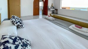 A bedroom with a bed, a bench, a wooden door, and a view of the sea through a window. - Surf-Check House - 3 min walk to the Beach (Playa del Hombre)
