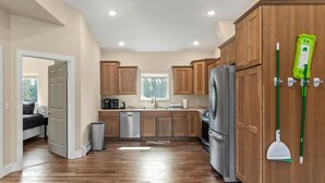 A modern kitchen with wooden cabinets, stainless steel appliances, and a green mop on the wall. - Modern Alaskan Retreat (Soldotna)