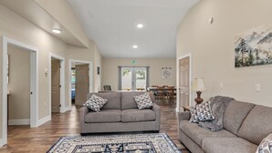 A spacious living area with a grey sofa, patterned cushions, a blue and white rug, and a painting of a mountain landscape on the wall. - Modern Alaskan Retreat (Soldotna)