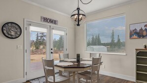 A dining area with a table set for four, a chandelier, a clock, and a 'HOME' sign above a door.