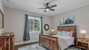 A bedroom with a wooden bed, a ceiling fan, a window with curtains, and a view of trees.