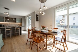 A modern kitchen with wooden chairs, a dining table set for four, and large windows offering a view of the mountains.