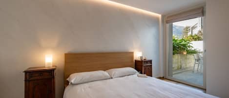 Un dormitorio con cabecera de madera, una cama grande, mesitas de noche con lámparas y una puerta corrediza de cristal a un balcón.