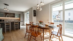 Ett modernt kök med trästolar, ett matbord för fyra personer och stora fönster med utsikt över bergen.