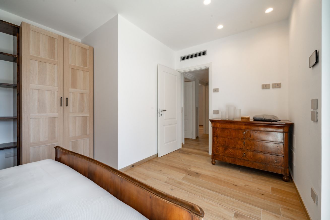 A bedroom with a wooden bed, a wardrobe, a dresser, and a door leading to another room.