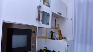A compact kitchen with a built-in microwave, a small oven, and a sink. There are cabinets with handles and a hanging light fixture. - Cozy Studio Near UN Base | 5-Min Drive to Entebbe Airport (Entebbe)