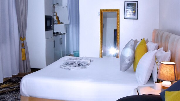 A hotel room with a bed, bedside table, lamp, air conditioning unit, and a mirror on the wall. - Cozy Studio Near UN Base | 5-Min Drive to Entebbe Airport (Entebbe)