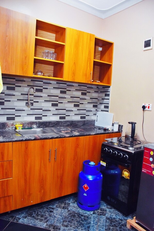 A kitchen with wooden cabinets, a tiled backsplash, a sink, a stove, and a gas cylinder.