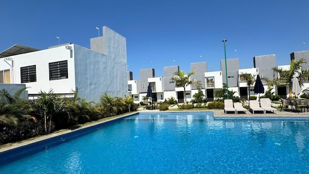 A swimming pool with lounge chairs and a modern building complex in the background. - Residencia Altavela Privada 51 (Valle de Banderas)