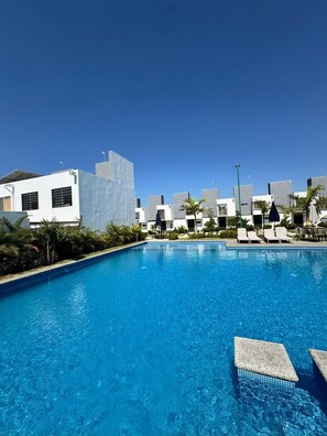 En pool med solstolar och en modern byggnadskomplex i bakgrunden.