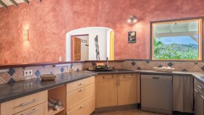 Uma cozinha com armários de madeira, bancada preta e vista para o verde lá fora.
