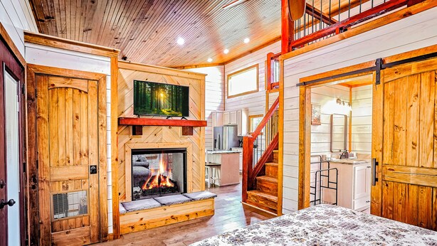 L’intérieur d’un chalet accueillant, avec une cheminée, des murs en bois, un lit et un escalier menant à un étage supérieur.