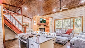 Un vaste espace de vie doté d’une cheminée, une cuisine équipée d’une cuisinière et un escalier.