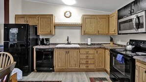 A kitchen with wooden cabinets, a black refrigerator, a microwave, a stove, and a sink. - Charming 2-bedroom in Florence within blocks of the beach, pet friendly, hot tub (Florence)