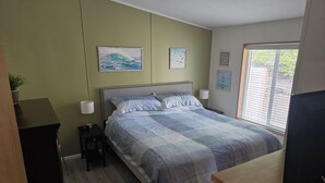 A bedroom with a bed, bedside tables, a lamp, and a window with blinds. - Charming 2-bedroom in Florence within blocks of the beach, pet friendly, hot tub (Florence)