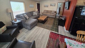 A living room with a grey sectional sofa, a wooden coffee table, and a red patterned rug. - Charming 2-bedroom in Florence within blocks of the beach, pet friendly, hot tub (Florence)