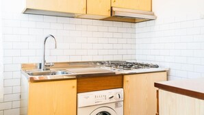 Cocina compacta con gabinetes de madera, pileta de acero inoxidable, estufa integrada y lavadora de carga frontal.