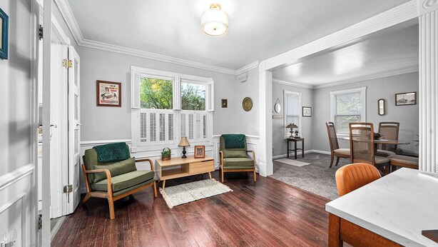 Uma sala de estar espaçosa com piso de madeira, uma área de jantar com mesa branca e uma cozinha com janela.