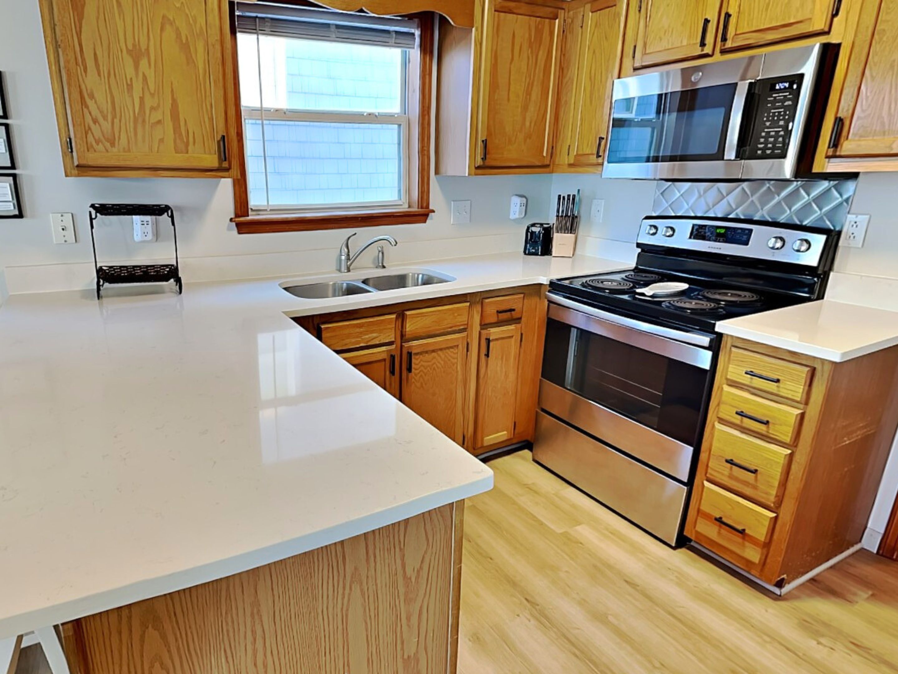 A kitchen with wooden cabinets, a stainless steel stove, a microwave, and a window with blinds.