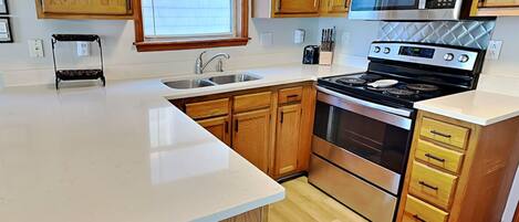 A kitchen with wooden cabinets, a stainless steel stove, a microwave, and a window with blinds.