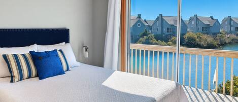 Habitación de hotel con una cama grande, vista a casas y agua desde un balcón.