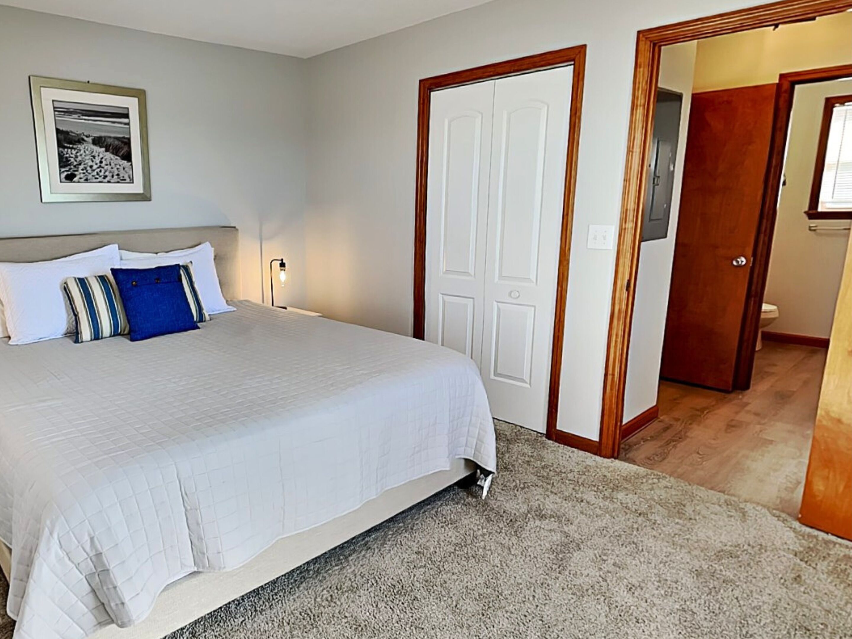 A bedroom with a large bed, a framed picture on the wall, and a door leading to a bathroom.