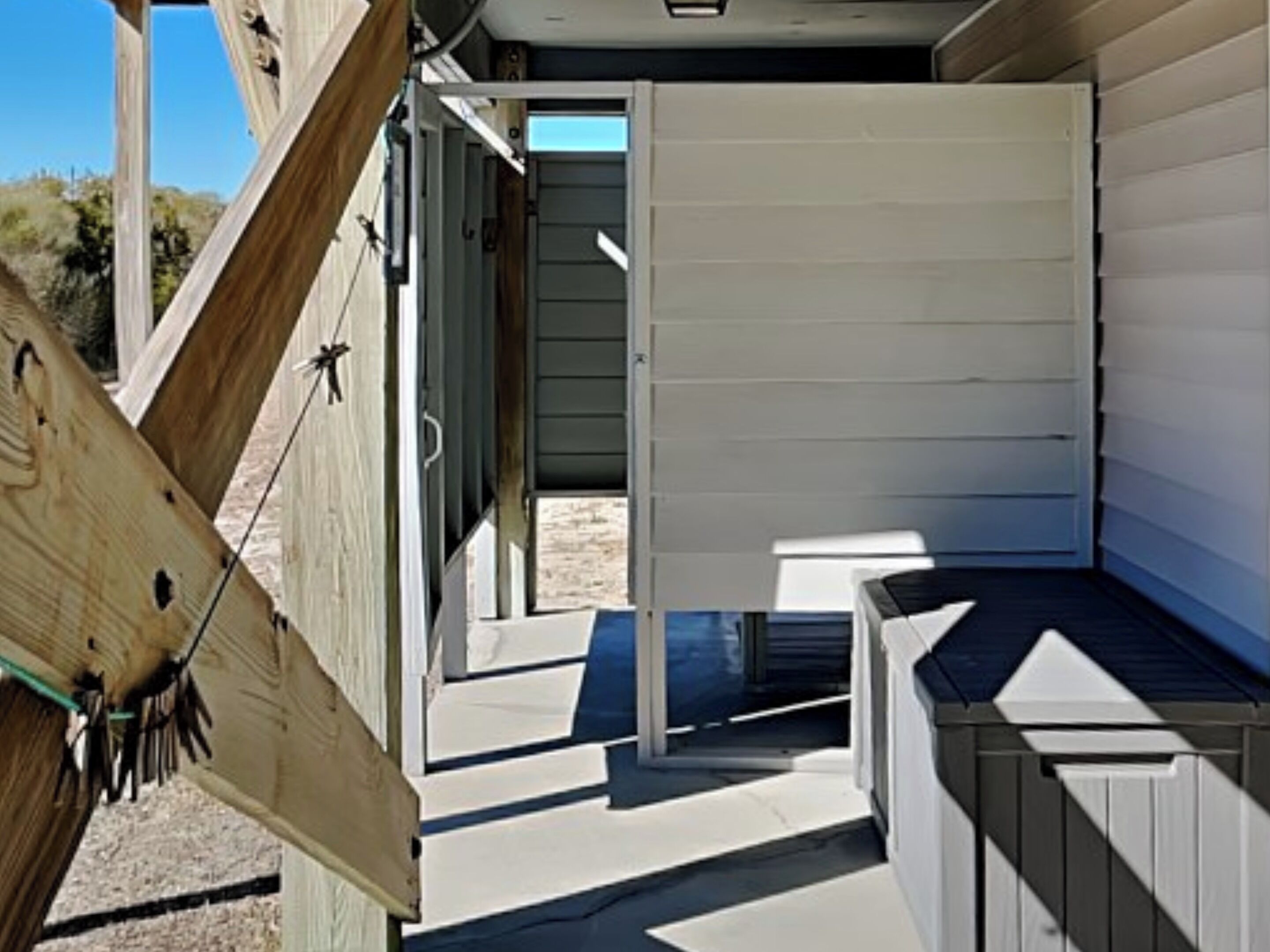 A narrow outdoor corridor with a wooden deck leading to a door, surrounded by white siding walls.