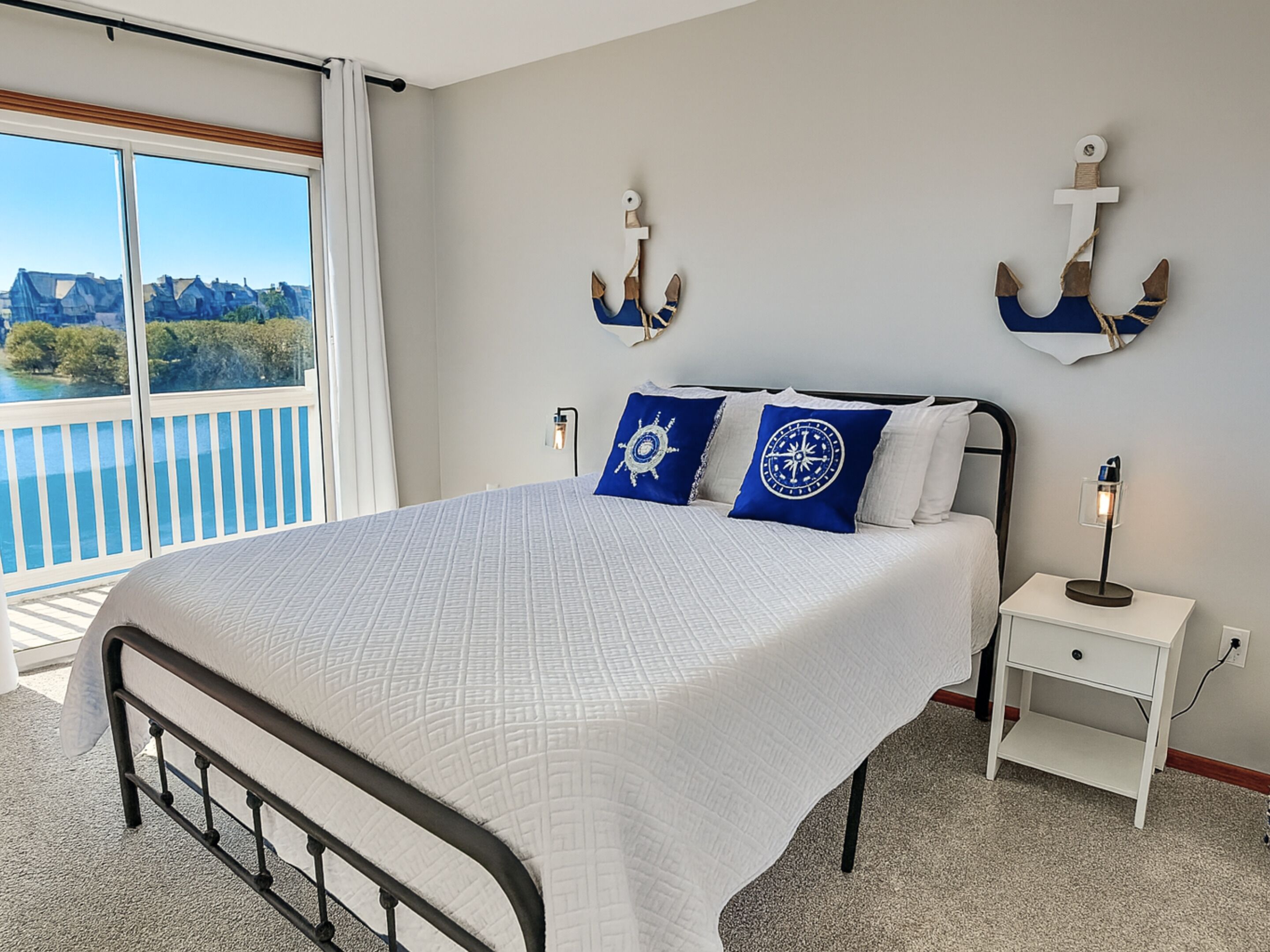 A bedroom with a bed, a nightstand, a wall-mounted anchor decoration, and a view of the outdoors.