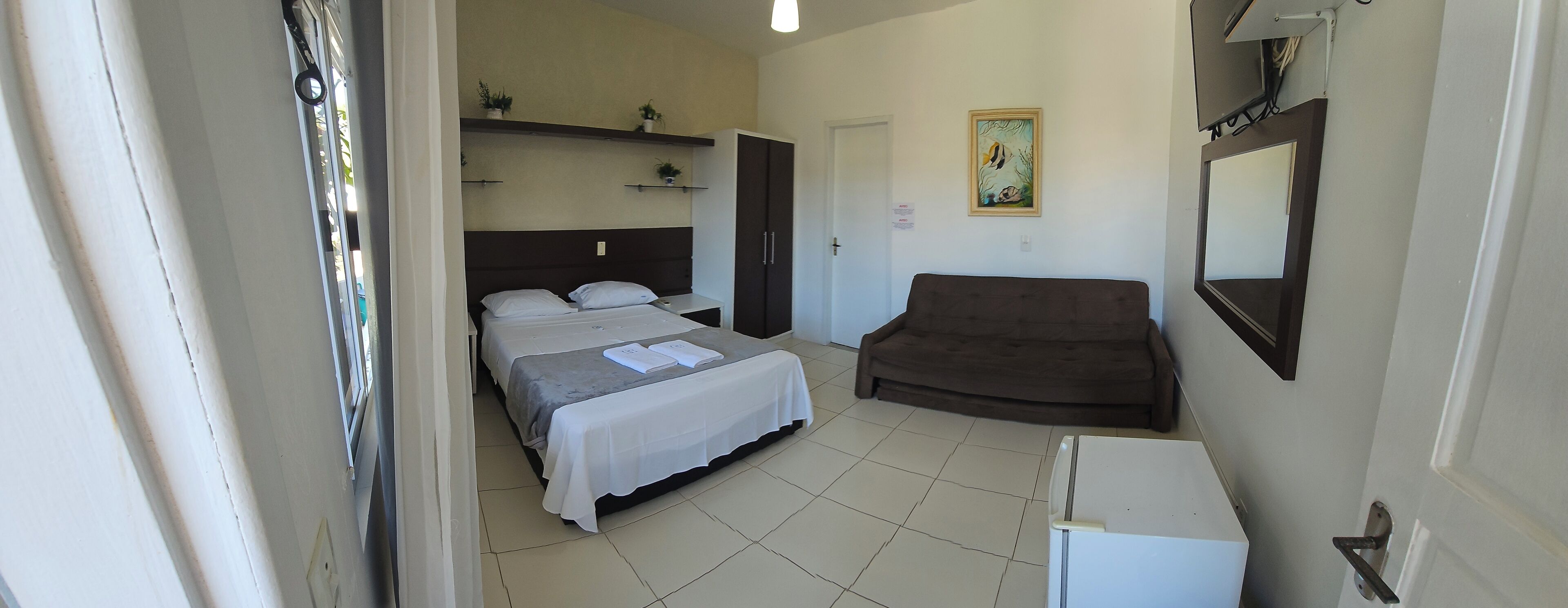 A bedroom with a bed, a dresser, a brown sofa, a small table, and a wall-mounted TV.