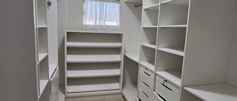 A walk-in closet with multiple shelves and drawers, a window with a sheer curtain, and a ceiling light.