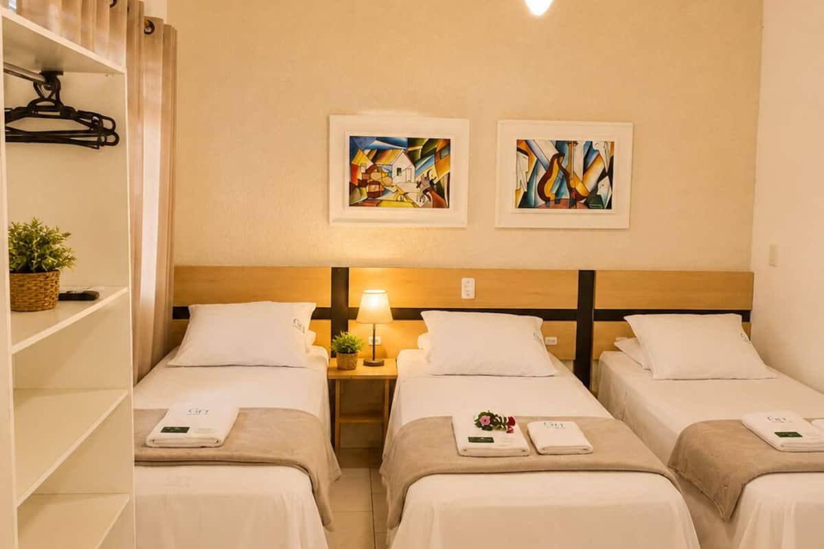 Habitación de hotel con dos camas, ventilador de techo, obras de arte en la pared y una estantería con una cesta y una toalla.