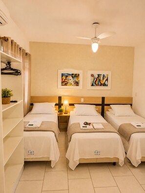 A hotel room with two beds, a ceiling fan, artwork on the wall, and a shelf with a basket and a towel. - GH Ingleses (Florianopolis)