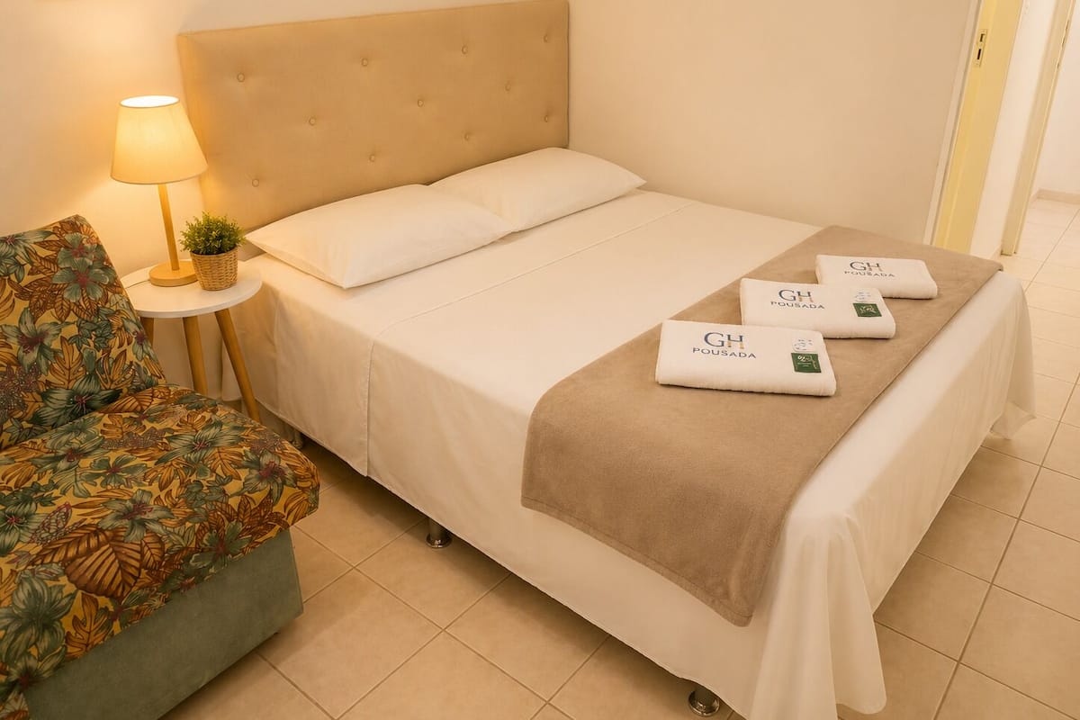 Habitación de hotel con cama, una silla, lámpara y toallas con el logotipo del hotel.