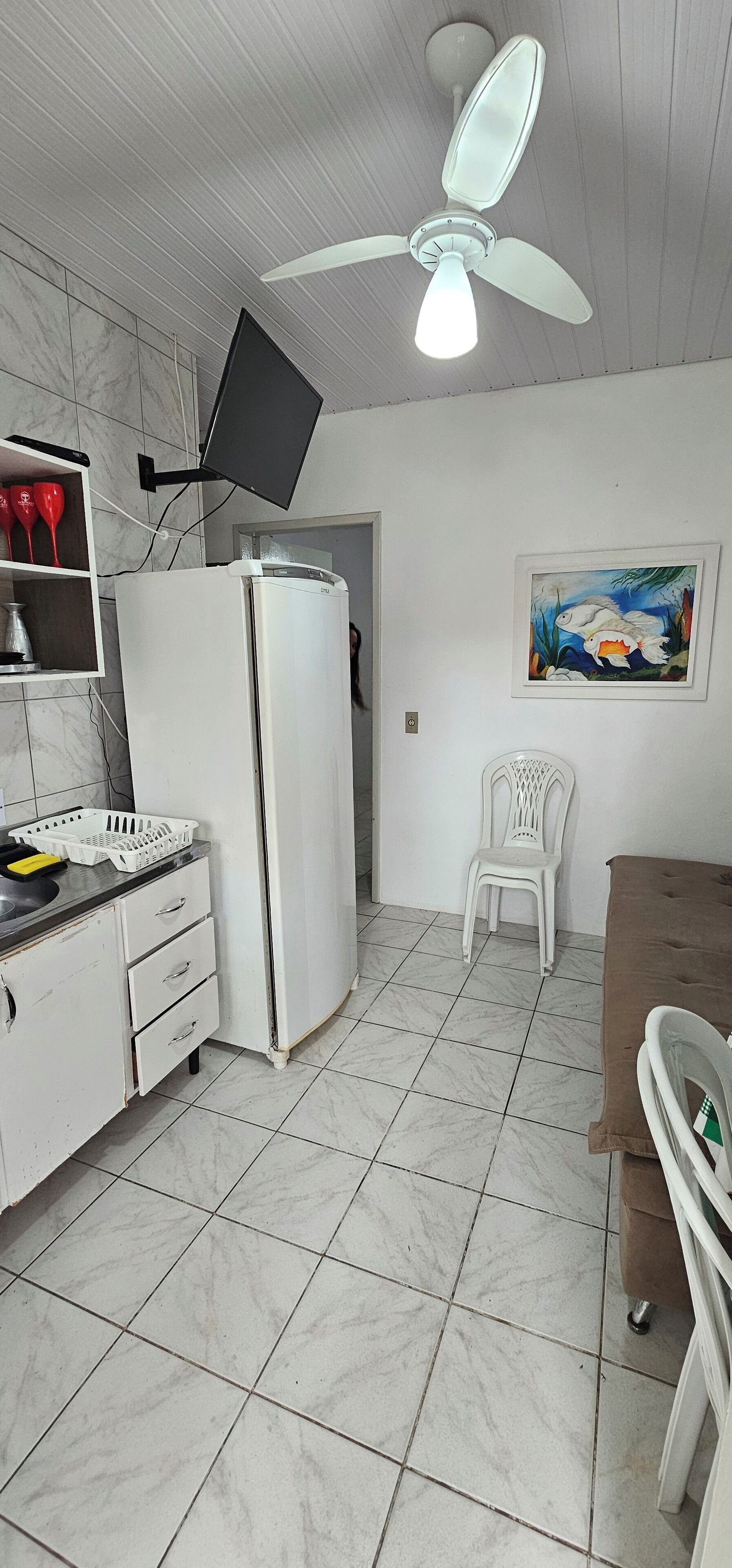 Eine Küche mit einem weißen Kühlschrank, einem Deckenventilator, einem an der Wand montierten Fernseher und einem Fischgemälde.