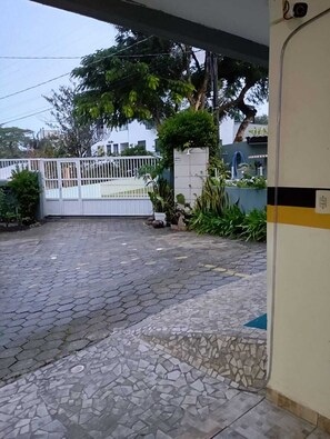 A paved courtyard with a white gate, surrounded by greenery and a building in the background. - GH Ingleses (Florianopolis)