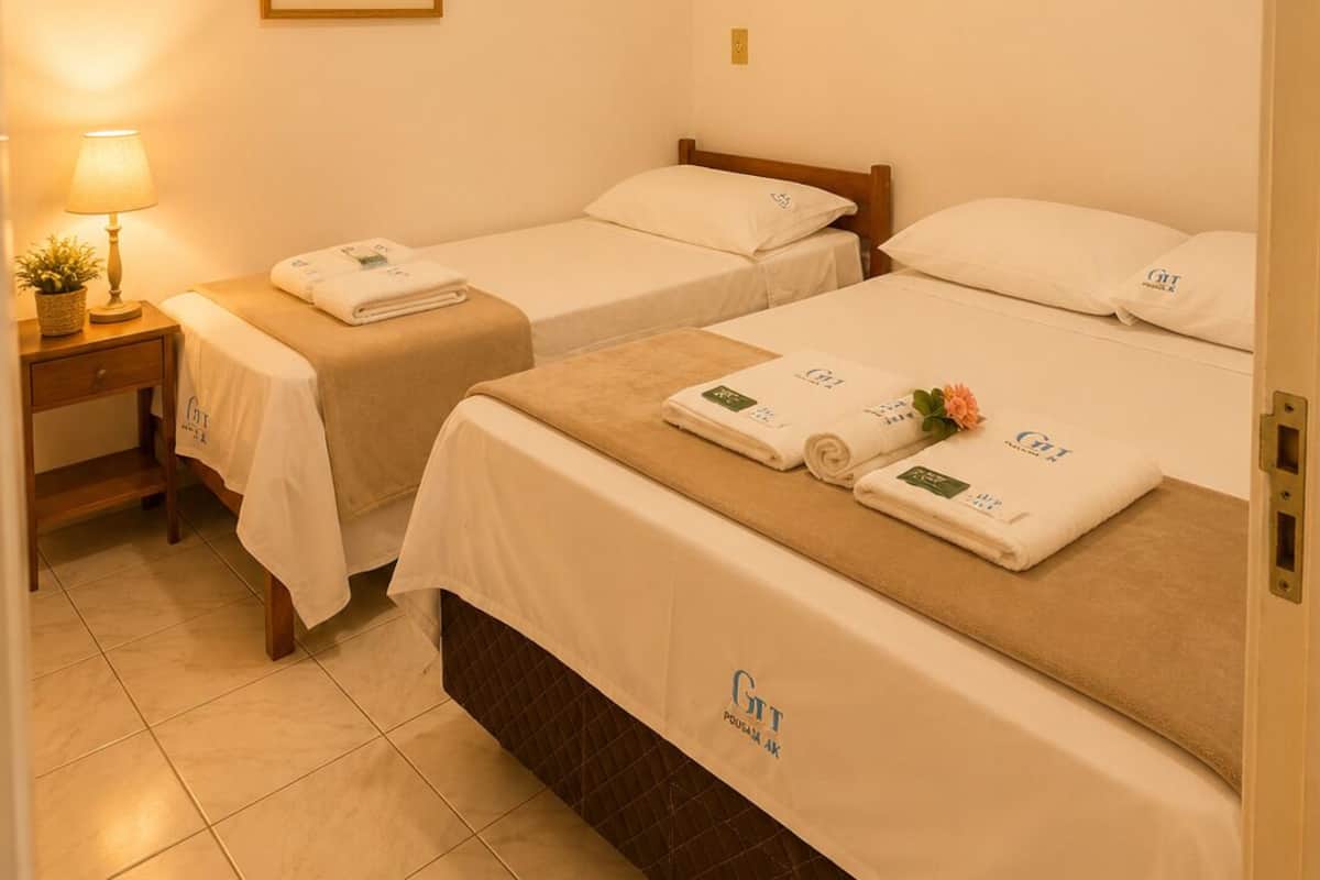 Una habitación de hotel con dos camas individuales, una mesita de noche con lámpara, una planta enmarcada en la pared y piso de baldosas.