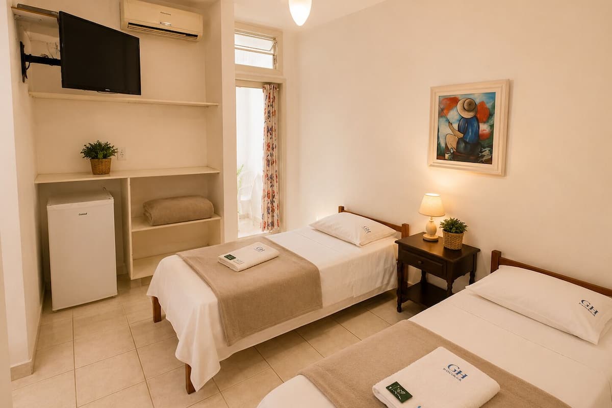 Habitación de hotel con dos camas, un escritorio, un refrigerador pequeño, un ventilador de techo y un cuadro en la pared.
