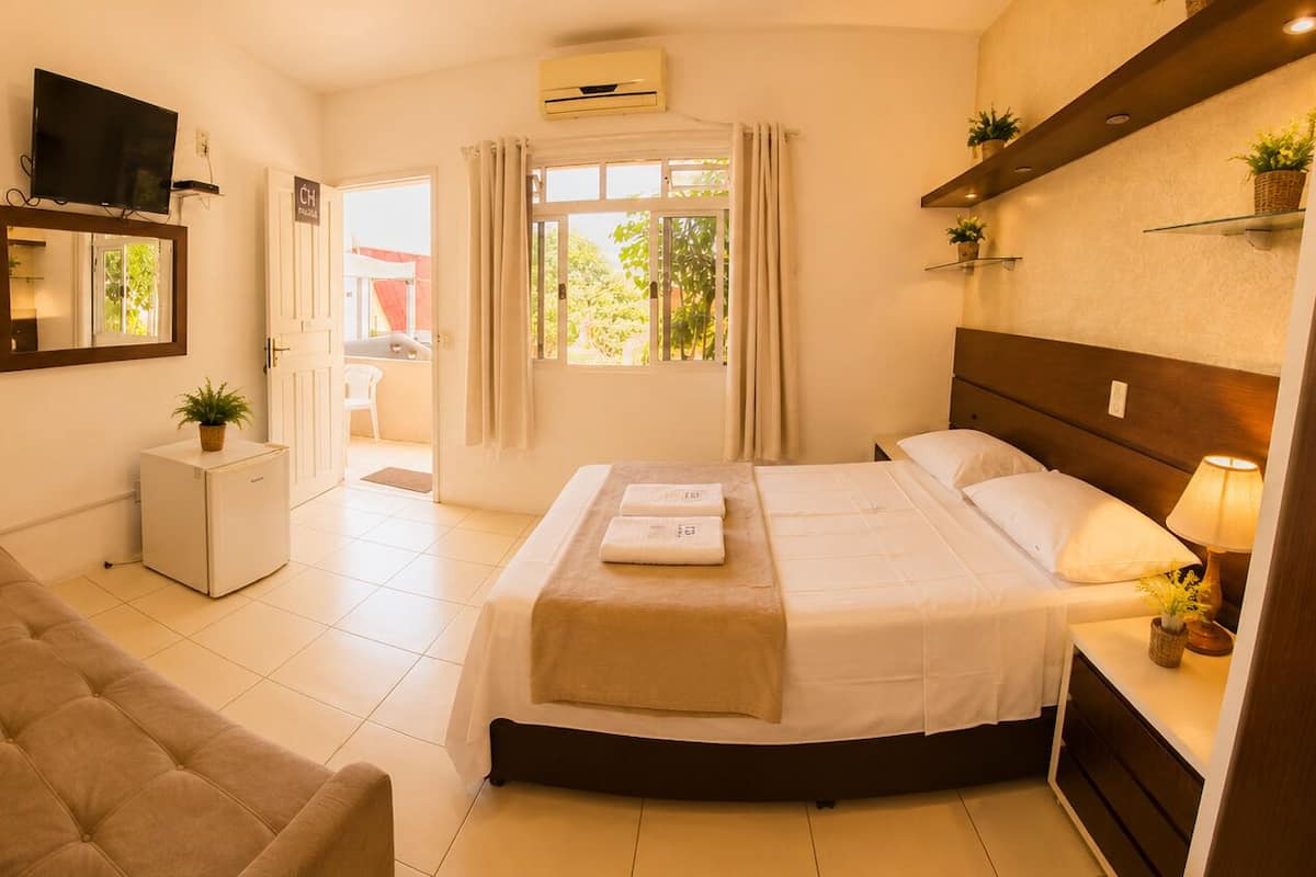 Habitación de hotel con cama, sofá, televisor, un refrigerador pequeño y ventana con cortinas.