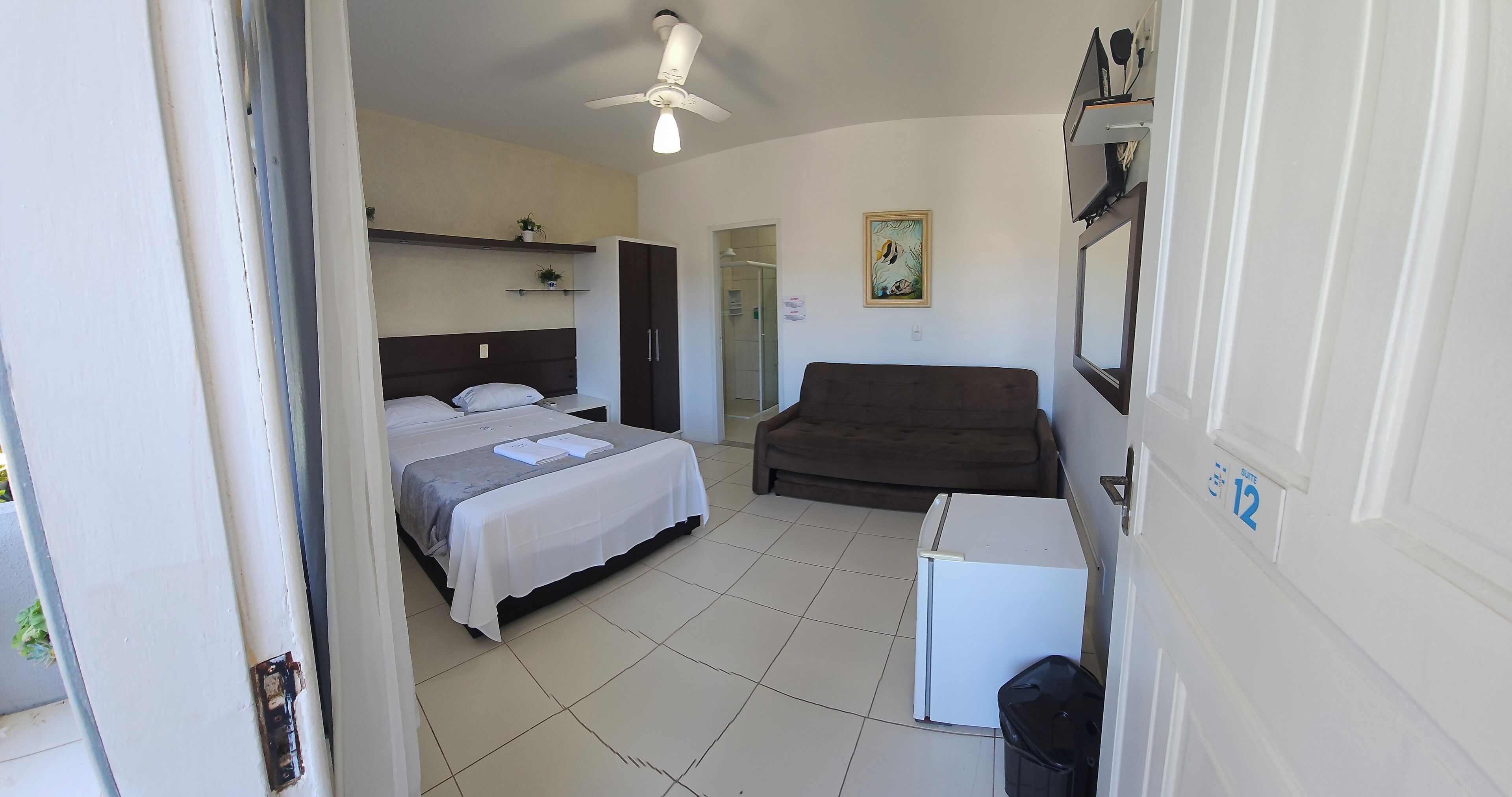 A bedroom with a bed, a small refrigerator, a sofa, and a ceiling fan.