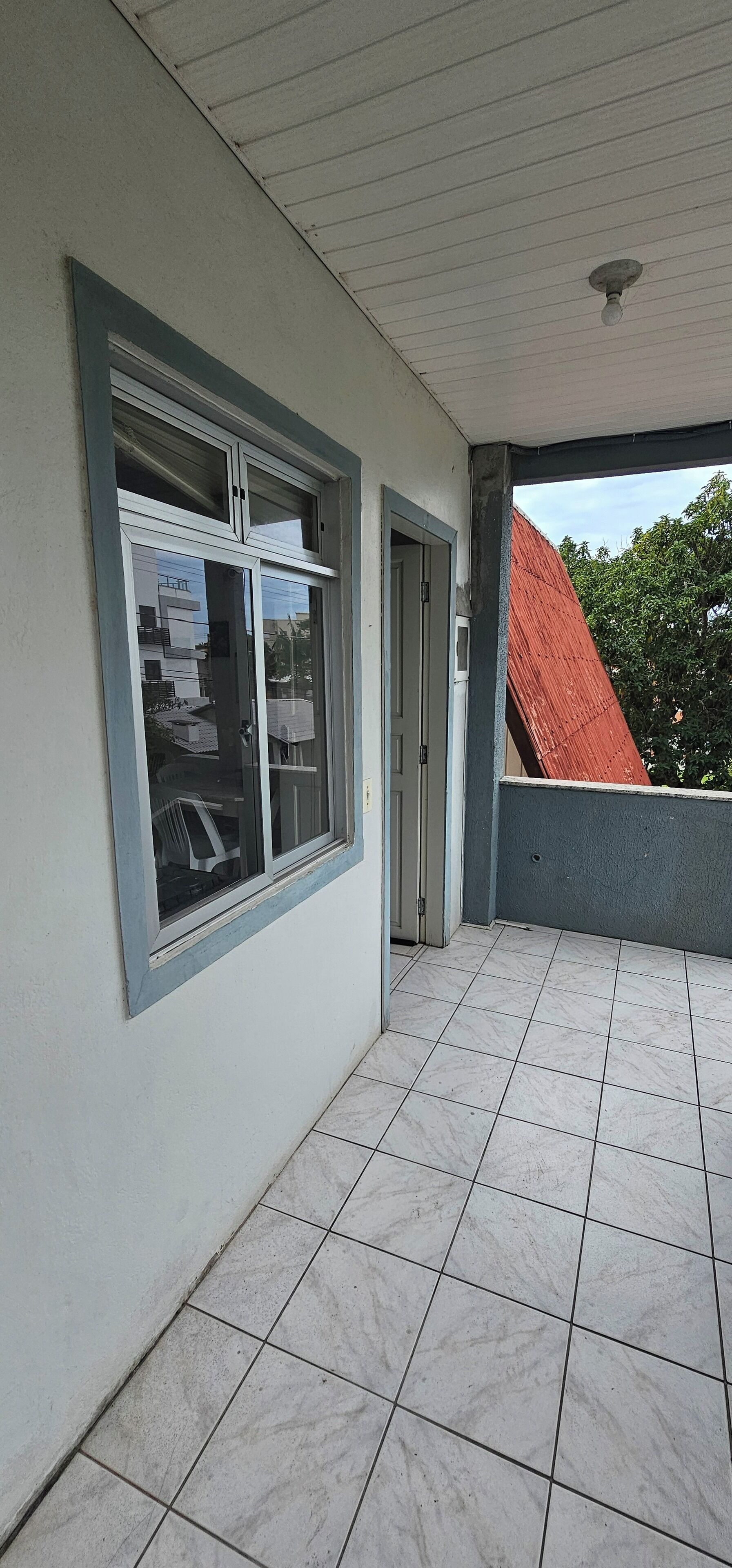 Un balcón cubierto con piso de baldosas, una ventana con persianas y una puerta.