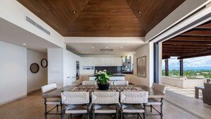 Un comedor amplio con techo alto y vistas a la cocina y al área de estar exterior.