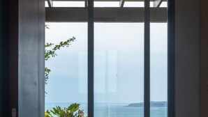 Una habitación con cama, una silla y vista al mar a través de amplios ventanales.