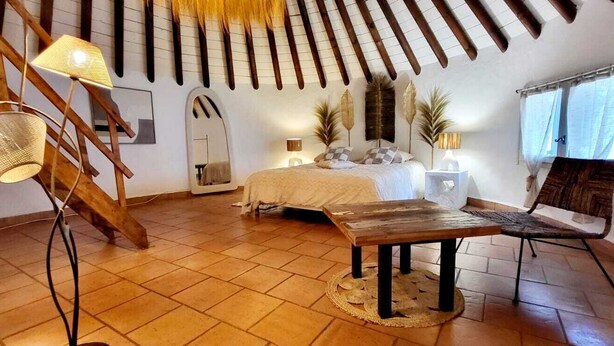 A bedroom with a bed, a wooden table, a chair, a staircase, and a window. - Cabane de Gardian unique in Petite Camargue Total disconnection unusual accommodation (Vestric et candiac)