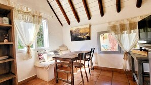 A rustic kitchen with wooden shelves, a wooden table, and chairs. There are windows with curtains, a painting on the wall, and a television on a stand. - Cabane de Gardian unique in Petite Camargue Total disconnection unusual accommodation (Vestric et candiac)