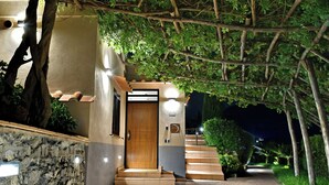 A well-lit entrance with a wooden door, stone wall, and steps leading to a covered area. - Mira Suite (Vietri sul Mare)