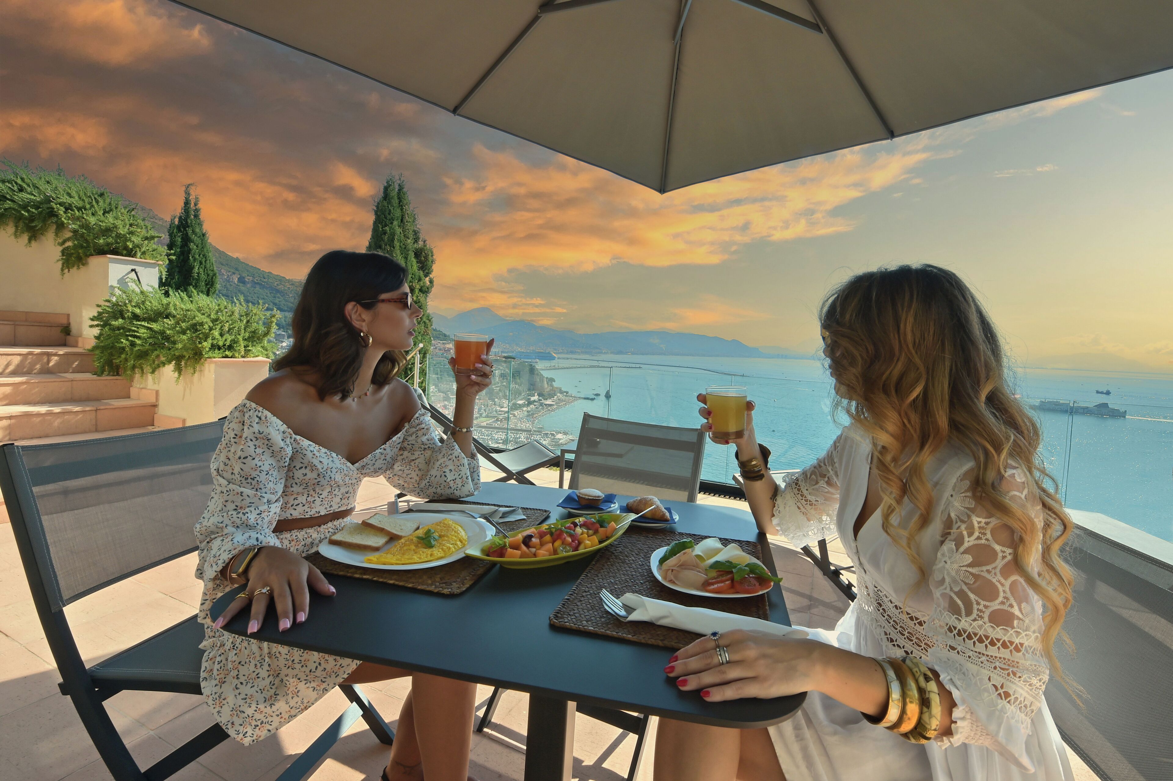 Two people dining at an outdoor table with a scenic view of the sea and mountains.